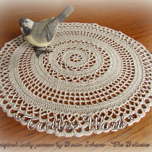 May include: A beige crocheted doily with a delicate, circular pattern. The doily is on a wooden surface with a small bird figurine on top. The text "Trellis Work" is written below the doily.