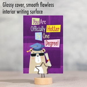 May include: A graduation card with a cartoon dog wearing a graduation cap and sunglasses. The card has a purple background with the text "You Are Officially Hotter By One Degree!" in yellow, red, and blue boxes.