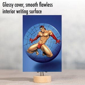 May include: A glossy, red and black illustrated postcard featuring a man in a red and black costume with a spider web design. The man is posed in a dynamic action pose.