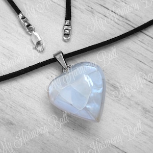 May include: A silver heart-shaped pendant necklace with a white iridescent stone. The necklace is on a black suede cord.