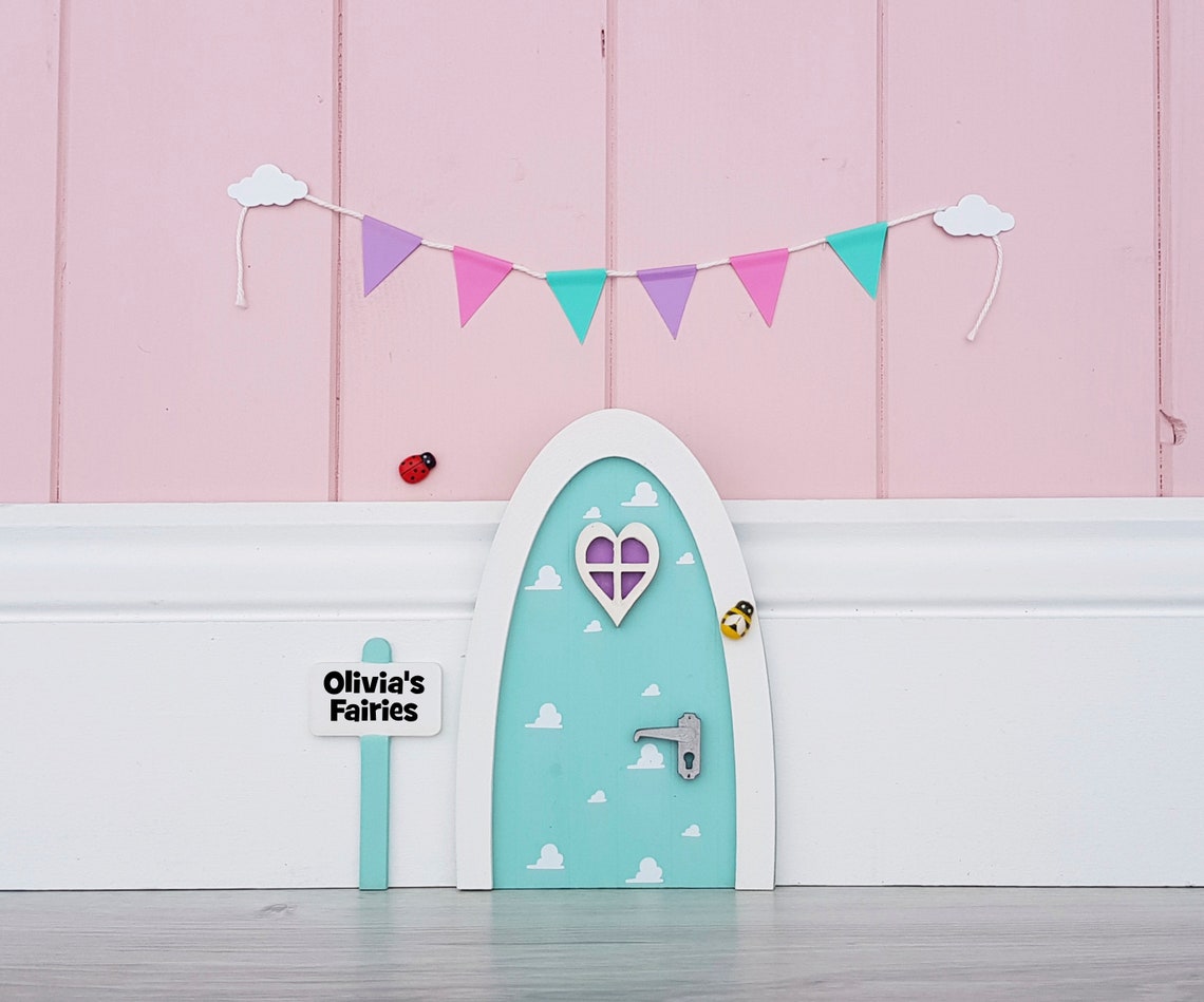 A light blue fairy door attached to a pink wall