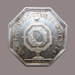 Puede incluir: Una medalla octogonal de plata con una inscripción que dice "Lex est quodcunque nota  illis." La medalla presenta un sol estilizado con una brújula y un globo terráqueo.
