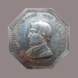 Puede incluir: Una medalla octogonal de plata con un retrato de Jean Rouvet, inventor de las balsas salvavidas. La medalla dice "Jean Rouvet Inventeur Des Flottages En 1791".