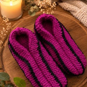 Peut inclure: Une paire de chaussons en crochet magenta vif avec une bande noire distincte courant le long du centre de chaque chausson. Les chaussons sont fabriqués avec un motif en maille texturée et présentent un bout arrondi avec une petite étiquette vert clair.