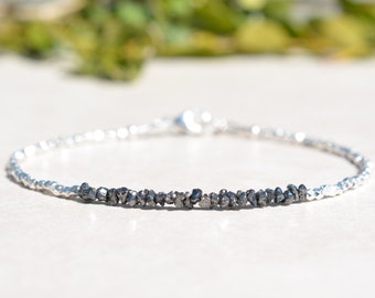 May include: A silver bracelet with a row of black rough diamonds in the center.
