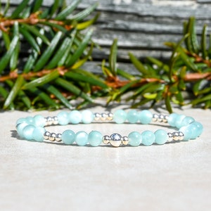 May include: A light blue gemstone bracelet with silver beads. The bracelet is made with small, round beads and has a larger silver bead in the center.