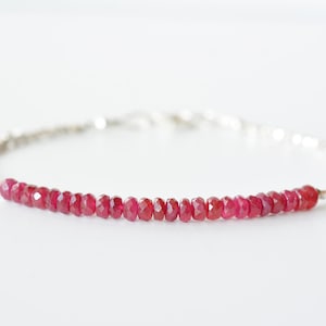 May include: A delicate silver chain bracelet with a row of small, faceted ruby red gemstones.