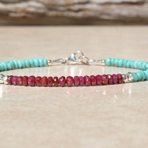 May include: A turquoise and ruby gemstone bracelet with a silver clasp. The bracelet is made with small, round beads.