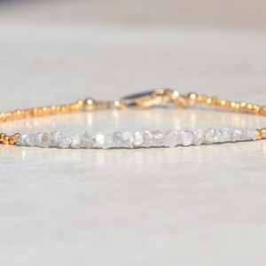 May include: A delicate gold bracelet with a row of small, rough-cut diamonds. The diamonds are set in a simple, elegant design, and the bracelet is finished with a gold clasp.