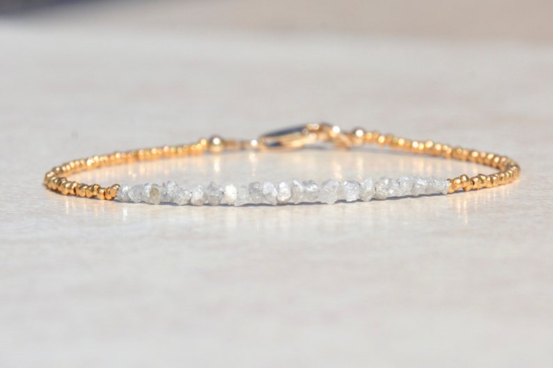 May include: A delicate gold bracelet with a row of small, rough-cut diamonds. The diamonds are set in a simple, elegant design, and the bracelet is finished with a gold clasp.