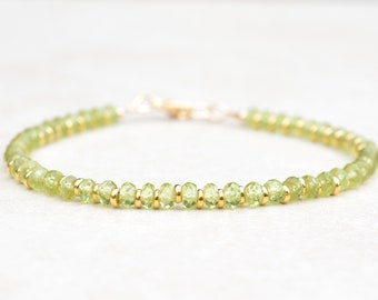 Puede incluir: Un delicado brazalete de piedras preciosas verdes con detalles dorados. El brazalete está hecho con pequeñas cuentas facetadas y tiene un diseño simple y elegante.