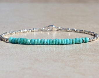 May include: A turquoise gemstone bracelet with a silver chain and clasp. The bracelet is made of small, round turquoise beads.