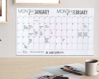 Könnte beinhalten: Ein weißer Trockenlöschkalender mit den Monaten Januar und Februar. Der Kalender enthält eine Liste von Ereignissen für jeden Tag. Der Kalender hängt an einer Wand über einem Schreibtisch mit einer Topfpflanze, gerahmten Fotos und einer Tasse.