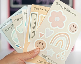 May include: A set of six sticker packs with various themes, including "Be Happy", "Back to School", "Sporty", "Doggie Buddies", and "Out of This World". The stickers feature a variety of designs, including rainbows, hearts, stars, and smiley faces. The sticker packs are beige and white with black text.