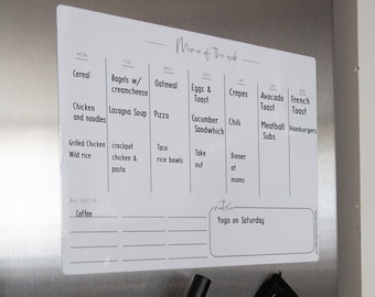 May include: A white dry-erase weekly meal planner with a black marker and a gray microfiber cloth hanging on a stainless steel refrigerator. The planner has a grid with days of the week labeled and meal ideas listed for each day. The text "Menu of the week" is at the top of the planner.