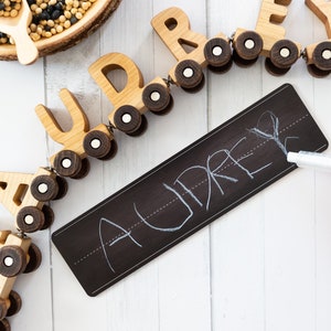 Peut inclure: Train en bois jouet avec les lettres AUDREY sur chaque wagon. Le train est sur une surface blanche avec un tableau noir qui dit AUDREY &eacute;crit dessus &agrave; la craie blanche.