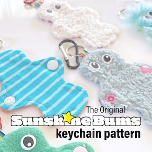 May include: Four colorful plush keychain patterns with a rainbow ribbon and a metal clasp. The text "The Original Sunshine Bums keychain pattern" is printed on the image.