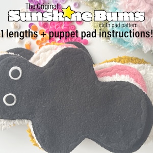 May include: A stack of 11 black, white, pink, and yellow cloth pads. The pads are shaped like a teardrop with rounded edges. The text "The Original Sunshine Bums cloth pad pattern 11 lengths + puppet pad instructions!" is printed above the pads.
