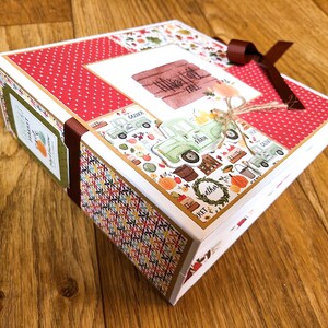 May include: A decorative box with a fall theme. The box features a red and white polka dot pattern, a brown ribbon, and a collage of fall-themed images, including pumpkins and a green truck. The text "Harvest Fall Free" is visible.