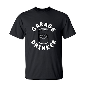 May include: Black t-shirt with white text that reads "Garage Drinker" and a graphic of a can of beer with the word "Beer" on it.