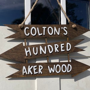May include: Three wooden arrow signs with white text. The top sign says "Colton's", the middle sign says "Hundred", and the bottom sign says "Aker Wood".