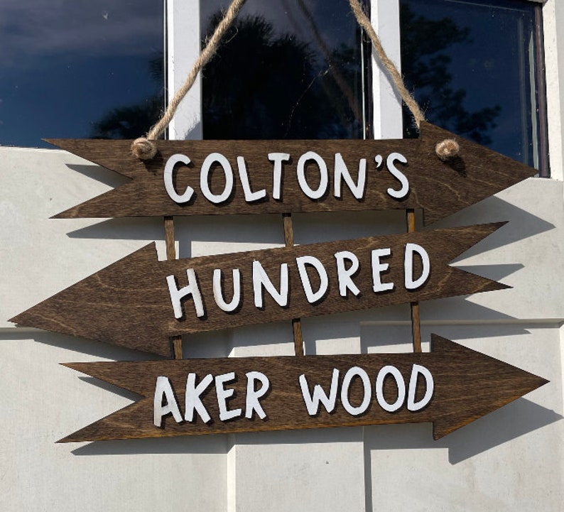 May include: Three wooden arrow signs with white text. The top sign says "Colton's", the middle sign says "Hundred", and the bottom sign says "Aker Wood".