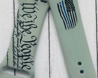 May include: A gray silicone watch band with a black and white print of the "We the People" portion of the US Constitution on one side and a blue line American flag on the other side.