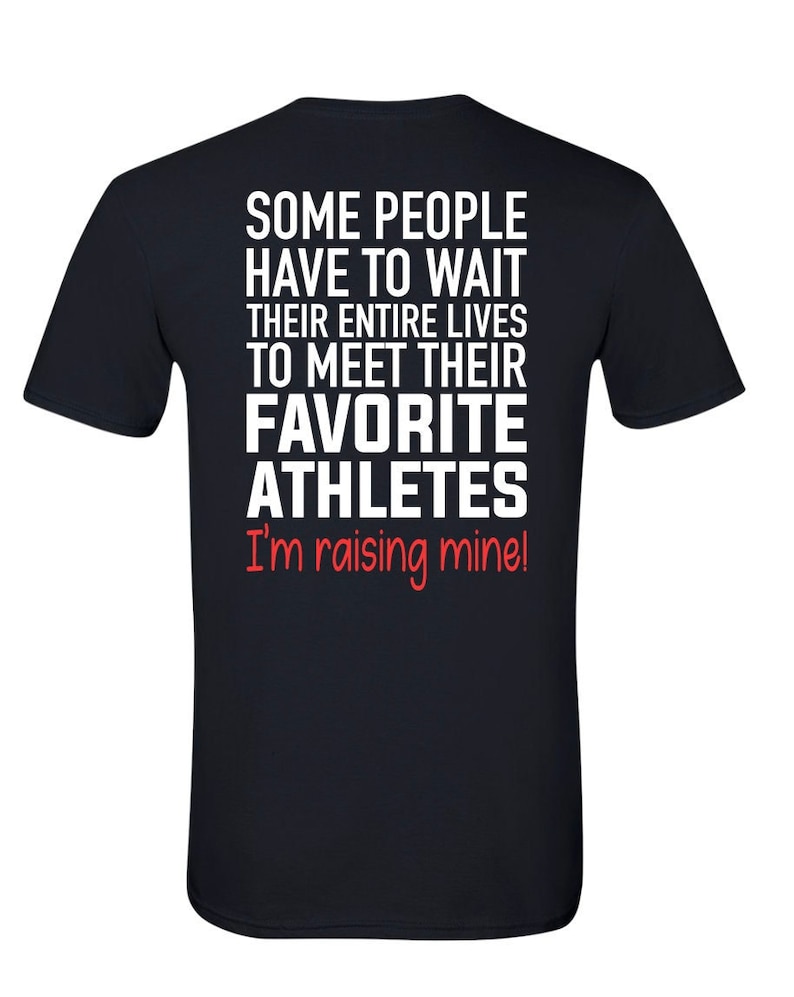 May include: Black t-shirt with white text that reads "Some people have to wait their entire lives to meet their favorite athletes. I'm raising mine!"