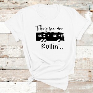 May include: White t-shirt with black text that reads "They see me rollin'...". A black silhouette of a recreational vehicle is above the text.