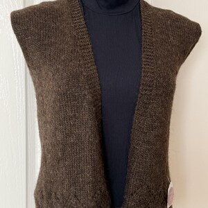 Pode incluir: Um cardigan de malha marrom sem mangas com decote em V e acabamento em renda. O cardigan é feito de um fio macio e felpudo.