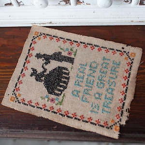 May include: A beige cross-stitch sampler with a black silhouette of two people holding hands. The text reads "A real friend is a treasure you can't buy".