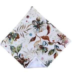 May include: A white square pillow with a floral pattern. The flowers are in shades of blue, green, and brown, and they are painted in a watercolor style. The background is a light cream color.