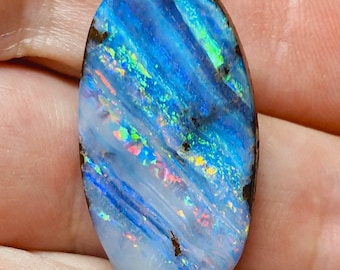 May include: An oval-shaped opal gemstone with a vibrant display of colors. The stone features a base of light blue and white, with streaks of darker blue and flashes of green, yellow, and red. The edges are a dark brown color.