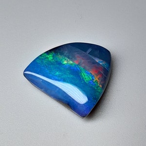 May include: A blue, green, and red iridescent opal cabochon with a curved, teardrop shape.