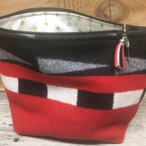 May include: A red, black, white, and gray patterned zippered pouch with a silver zipper pull and a tassel. The pouch is lined with a white fabric with gold arrows.