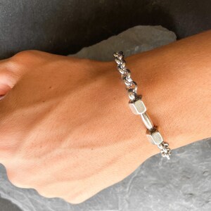May include: A silver chain bracelet with two silver dumbbell charms.