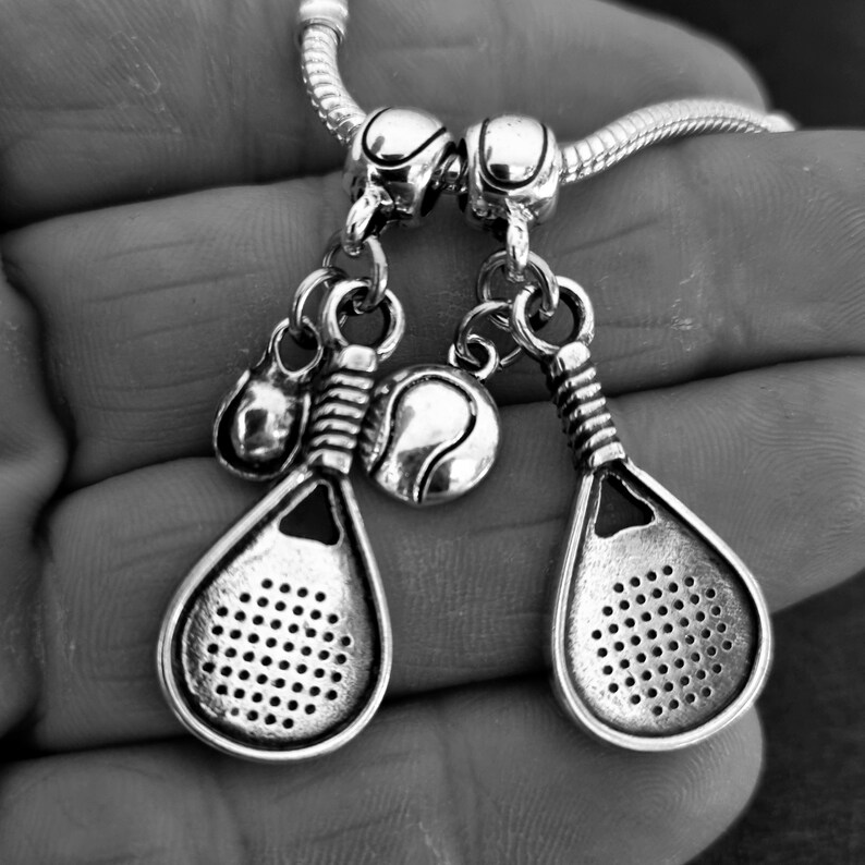May include: Silver charm bracelet with two silver paddle tennis racquet charms and a silver tennis ball charm.