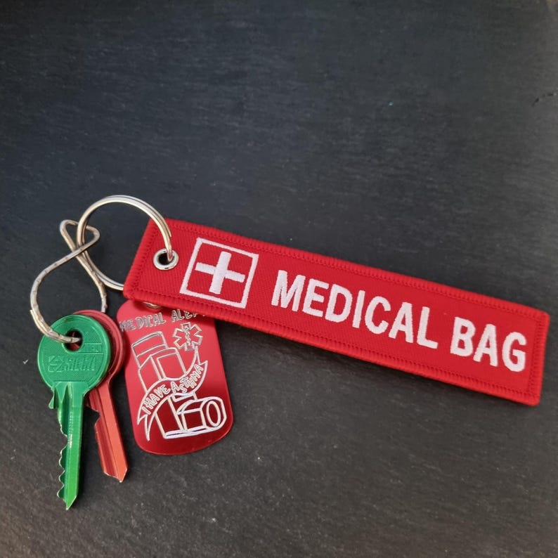 K&ouml;nnte beinhalten: Roter Schl&uuml;sselanh&auml;nger mit einem wei&szlig;en "MEDICAL BAG"-Etikett und einem roten Metalletikett mit einem wei&szlig;en medizinischen Warnsymbol und dem Text "I HAVE A SPRAY".