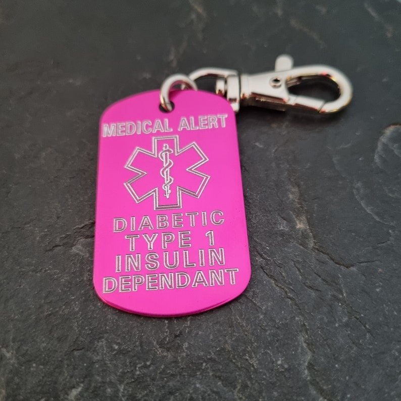 May include: Pink medical alert tag with a silver keychain. The tag has a star of life symbol and the text "MEDICAL ALERT", "DIABETIC TYPE 1 INSULIN DEPENDANT".