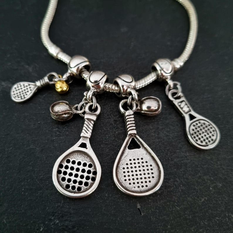 May include: A silver charm bracelet with tennis-themed charms, including rackets and balls. The charms are attached to a silver chain.