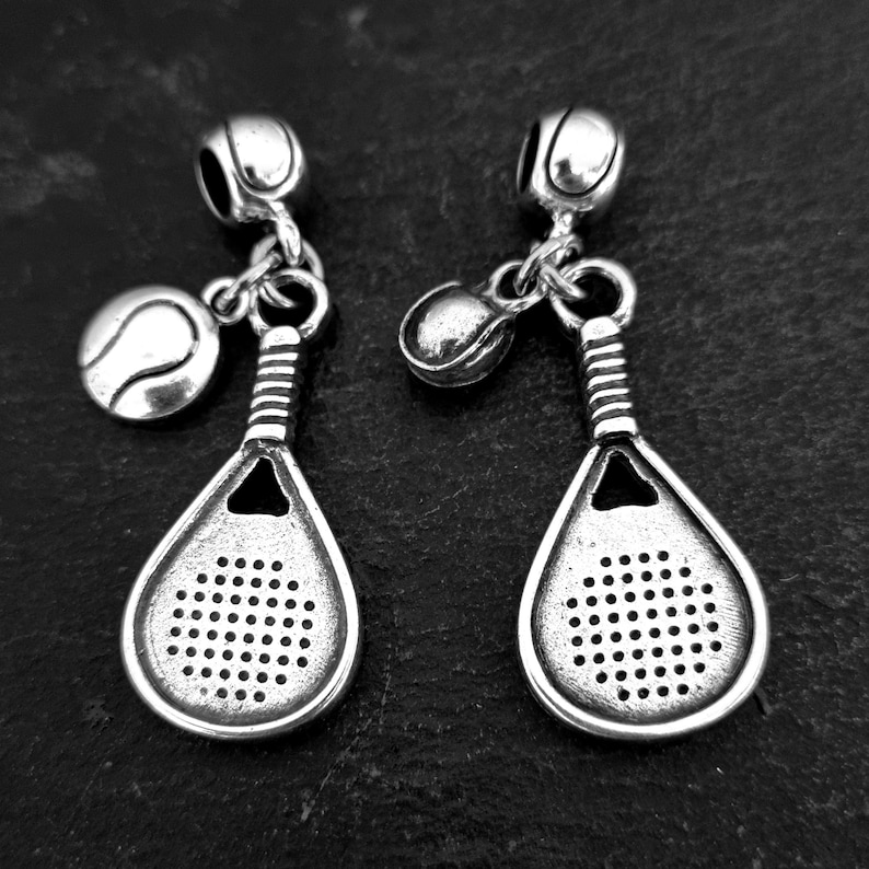 May include: Two silver charm bracelets with a tennis racket and tennis ball charms. The charms are detailed and have a vintage look.