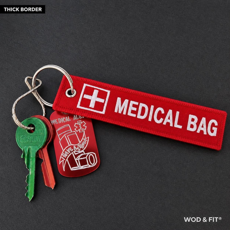 May include: A red rectangular fabric keychain with a white medical cross and the text MEDICAL BAG in white embroidery. Attached to a metal ring are a green key, a red key, and a red metal tag featuring a white asthma inhaler graphic.