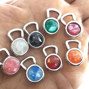 May include: Assortment of ten silver charm pendants with different coloured round glass inserts. The charms are shaped like a small kettlebell.