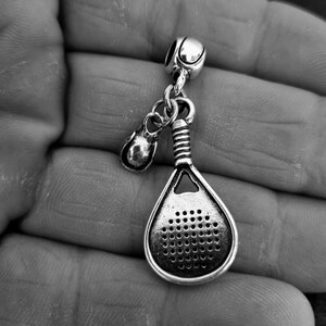 May include: A silver charm featuring a paddle and a small ball, likely for a bracelet or necklace.
