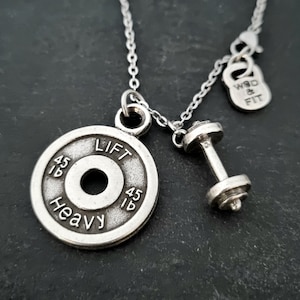 Peut inclure: Collier en argent avec un pendentif en forme de plaque de poids qui dit "Lift Heavy 45 lb" et un charme en forme d'haltère. Le collier a également un petit charme qui dit "WOD & FIT".