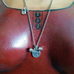 May include: Silver necklace with a weight plate pendant. The plate has the text "15 LBS 7 KG" on it. The necklace also has a small charm with the text "WKD & FIT" on it.