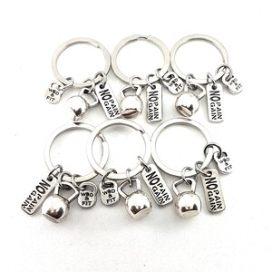 Puede incluir: Seis llaveros plateados con un dije de kettlebell y una etiqueta que dice "No Pain No Gain". Un llavero tiene una etiqueta que dice "WOD & Fit".