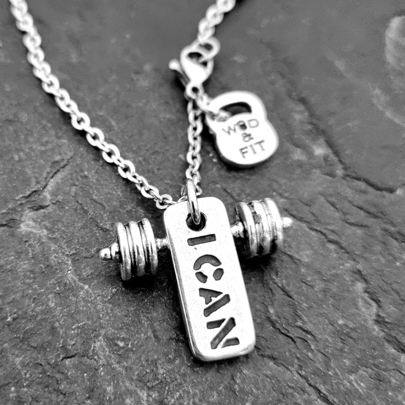 May include: Silver necklace with a dumbbell charm that says "I CAN" and a small silver charm that says "WOD & FIT".