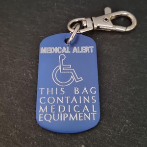 May include: Blue metal keychain with a silver clip. The keychain has the text "MEDICAL ALERT" and a wheelchair symbol. The text "THIS BAG CONTAINS MEDICAL EQUIPMENT" is also engraved on the keychain.