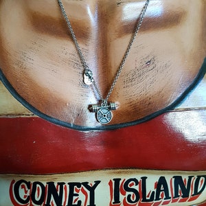 May include: A silver necklace with a barbell weight charm. The charm has a black weight plate with the words "LBS" and "2.5" printed on it. The necklace is on a mannequin wearing a red and white striped shirt with the words "CONEY ISLAND" printed on it.